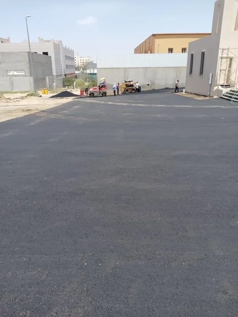 عمال ومعدات صغيرة أثناء سفلتة ساحة واسعة بين المباني