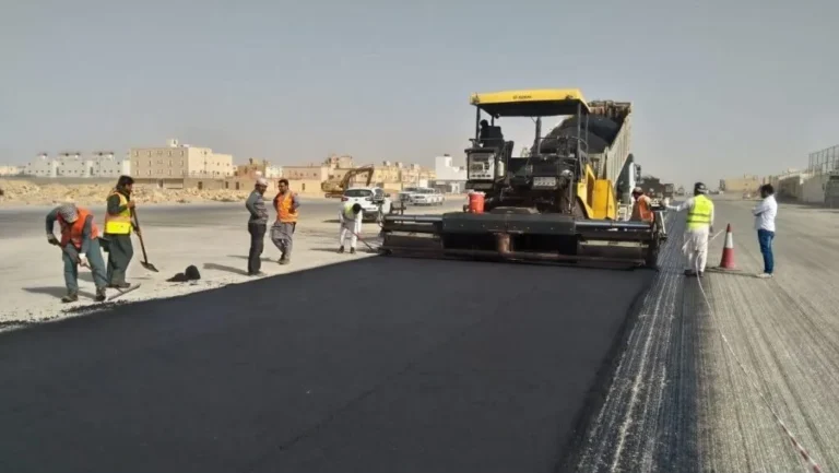 ماكينة فرد الأسفلت وعمال الموقع أثناء سفلتة شارع واسع
