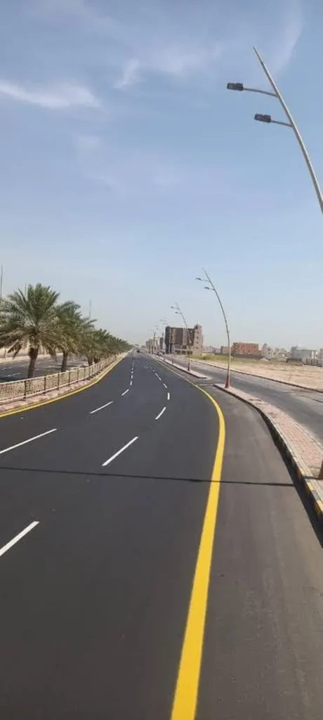 طريق مسفلت حديثاً بخطوط تخطيط بيضاء وصفراء وأعمدة إنارة
